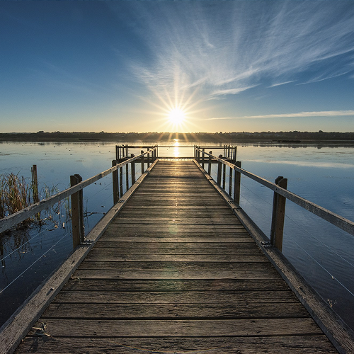 Holzsteg führt über ruhigen See zum Sonnenuntergang am Horizont