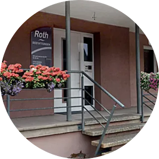 Eingang eines Gebäudes mit Schild 'Roth Bestattungen' neben der Tür und Blumenkästen mit roten und violetten Blumen